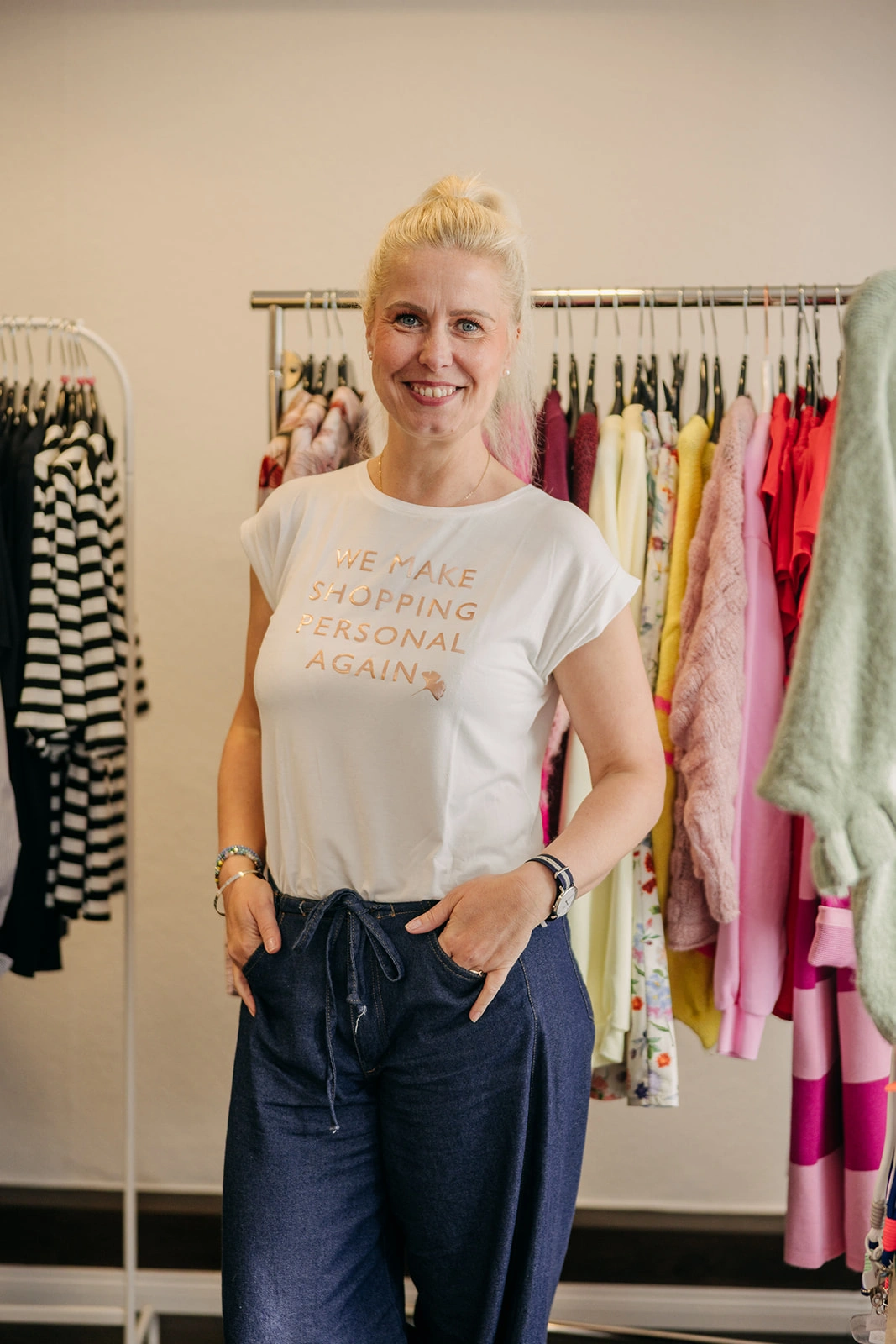 Cindy Franitzek steht lächelnd vor einer bunten Auswahl an Kleidungsstücken in ihrem Modegeschäft in Bispingen