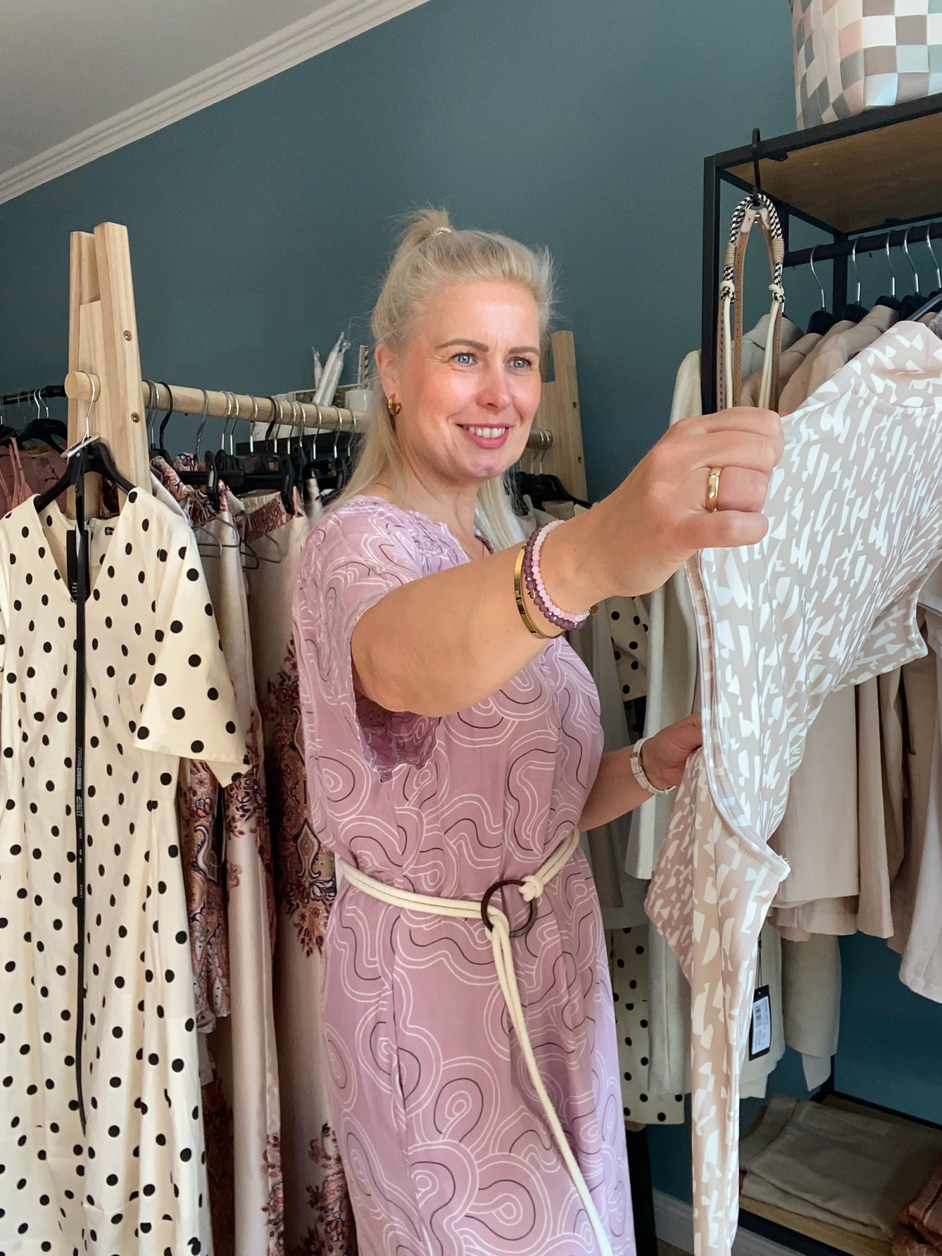 Cindy hält ein Kleidungsstück hoch und betrachtet es in ihrem Laden