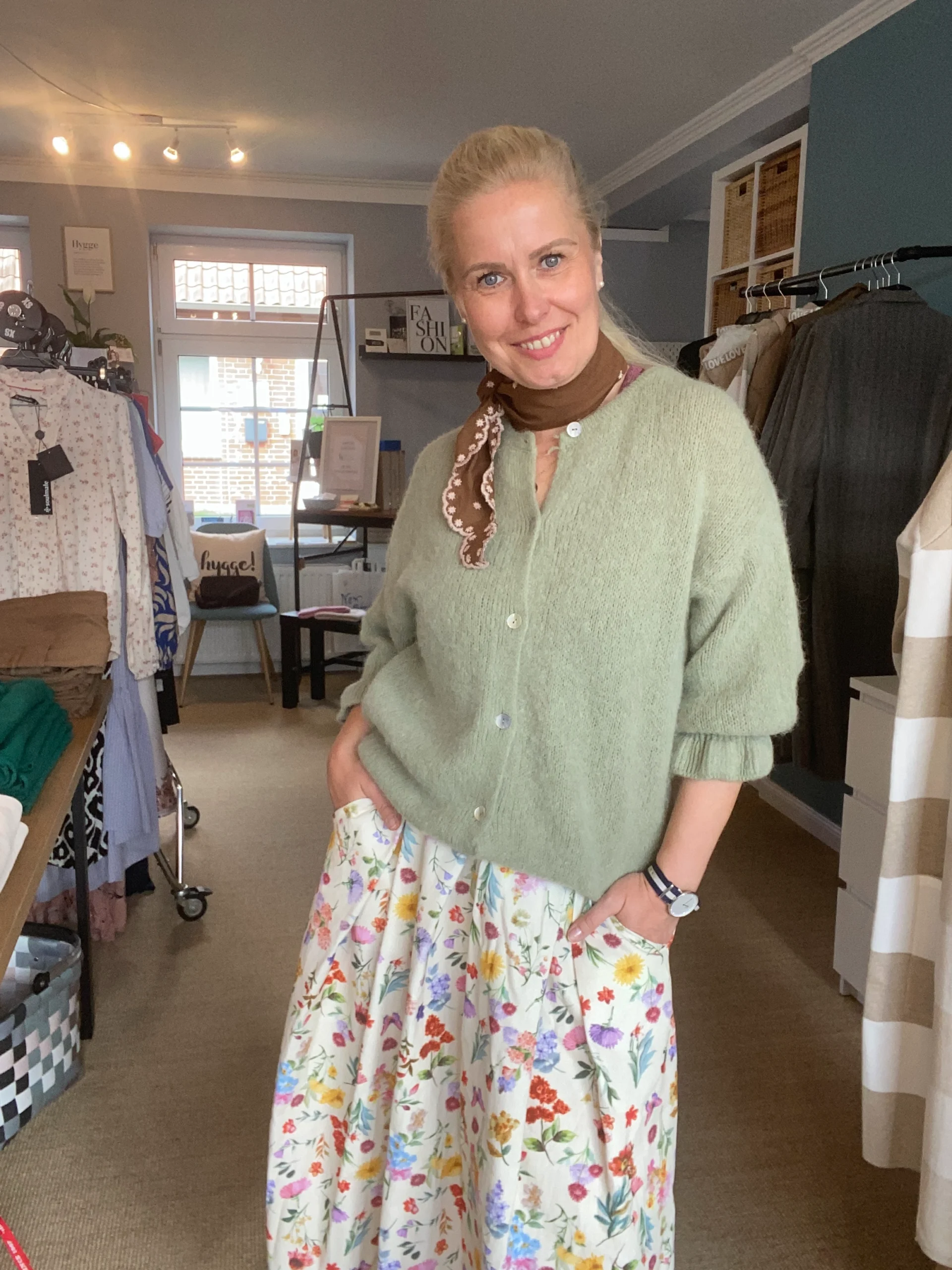 Cindy lacht in ihrem Laden, Kleidung im Hintergrund sichtbar